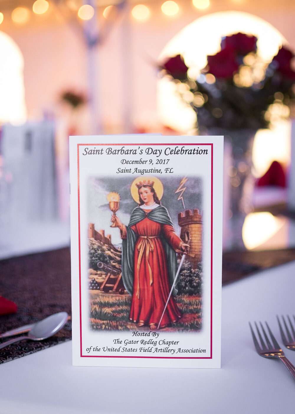 Program booklet for the Gator Redleg Chapter's Saint Barbara's Day Celebration, December 9, 2017, in St. Augustine, Florida, on a candlelit banquet table.